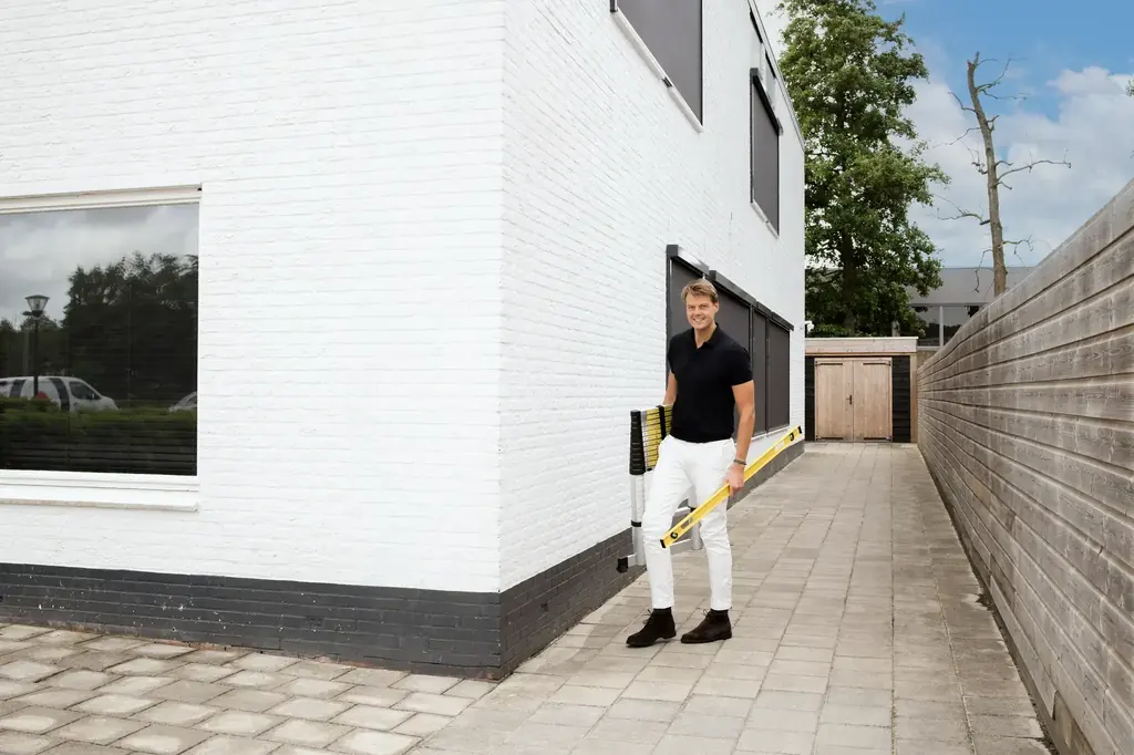 Persoon met een waterpas bij de gevel van een woning